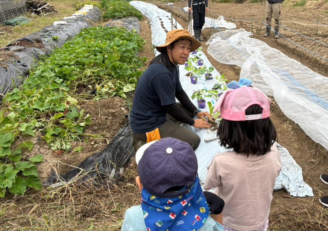 子どもたちと目線を合わせ、畑で苗植えについて説明する外薗明博